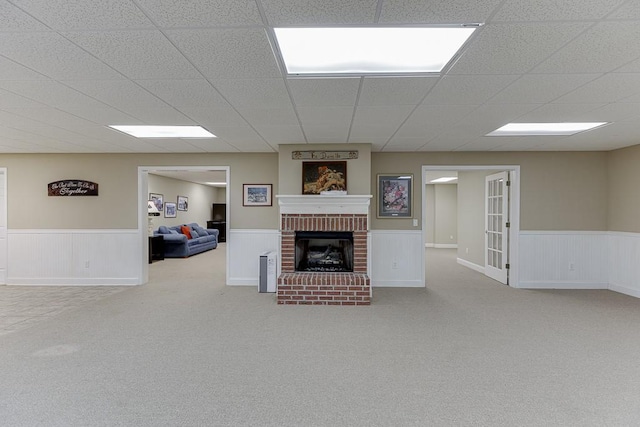 carpeted living area with a paneled ceiling, a wainscoted wall, and a fireplace