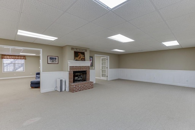 unfurnished living room with a paneled ceiling, a wainscoted wall, carpet, and a fireplace