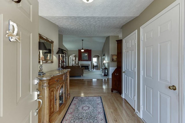 hall featuring light wood-style floors, lofted ceiling, arched walkways, and a textured ceiling