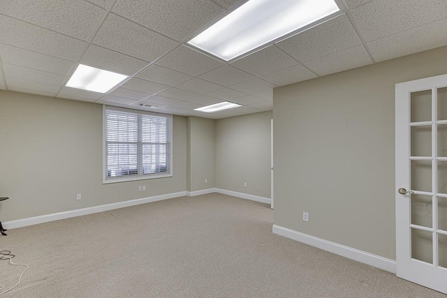 spare room with baseboards, a drop ceiling, and light colored carpet