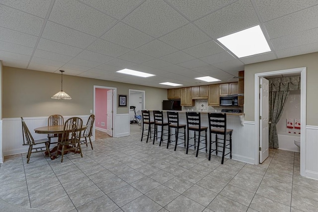 kitchen with pendant lighting, light countertops, wainscoting, a peninsula, and black appliances