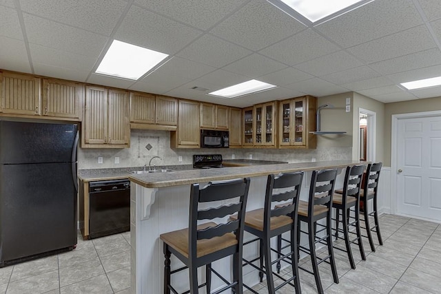 kitchen with a breakfast bar area, open shelves, glass insert cabinets, a sink, and black appliances