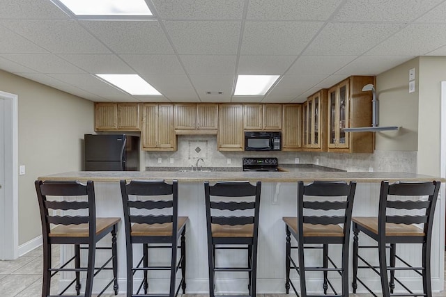 kitchen with a breakfast bar area, light countertops, decorative backsplash, black appliances, and glass insert cabinets