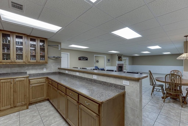 kitchen featuring dark countertops, visible vents, glass insert cabinets, light tile patterned flooring, and a peninsula