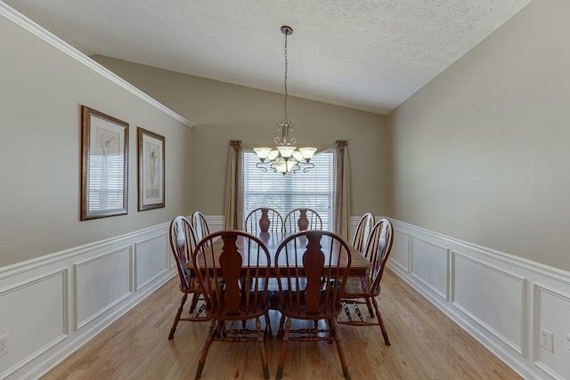 dining room with a decorative wall, vaulted ceiling, a textured ceiling, a chandelier, and light wood-type flooring