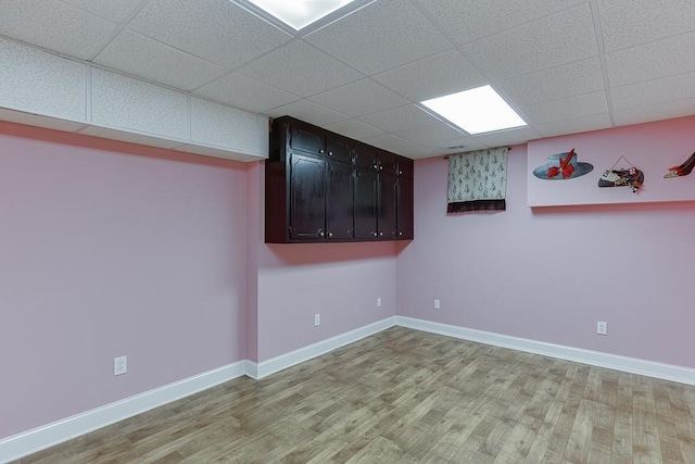 empty room featuring light wood-style floors, a drop ceiling, and baseboards