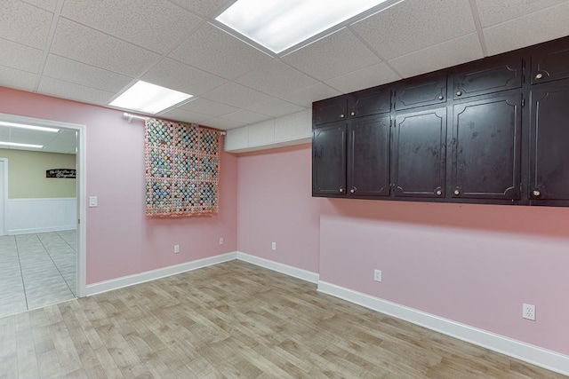 empty room with baseboards, a drop ceiling, and light wood-style floors