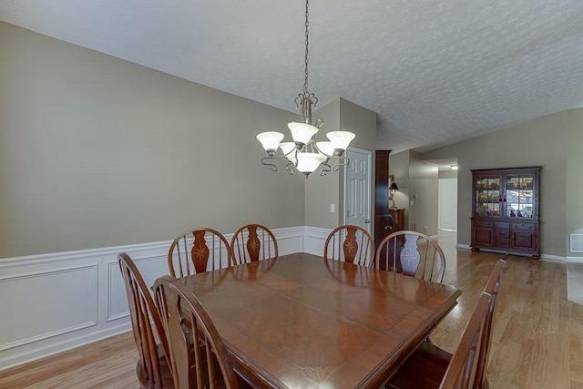 dining room featuring lofted ceiling, a notable chandelier, a textured ceiling, and light wood finished floors