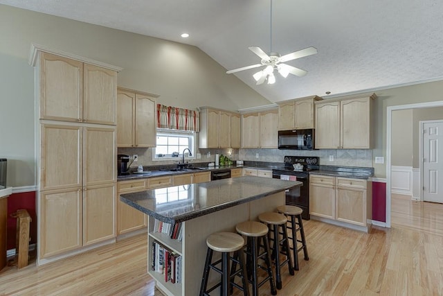 kitchen with a breakfast bar area, light brown cabinetry, a sink, a kitchen island, and black appliances