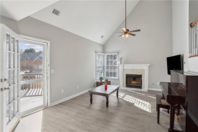 living room with a fireplace, ceiling fan, wood finished floors, baseboards, and high vaulted ceiling