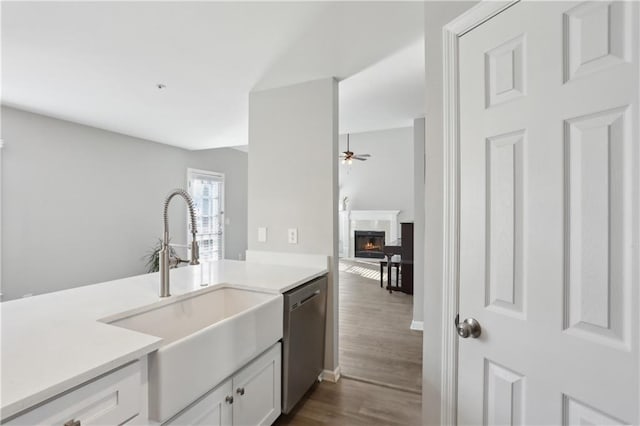kitchen with dishwasher, a sink, a ceiling fan, dark wood-type flooring, and a warm lit fireplace
