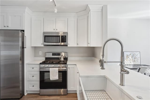 kitchen with appliances with stainless steel finishes, white cabinets, light countertops, a sink, and rail lighting