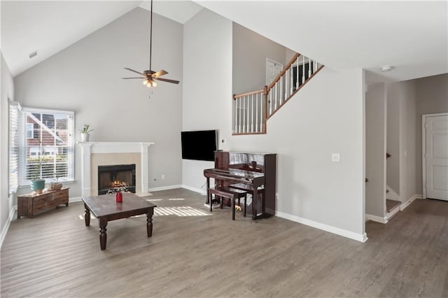 living area with wood finished floors, high vaulted ceiling, a premium fireplace, and ceiling fan