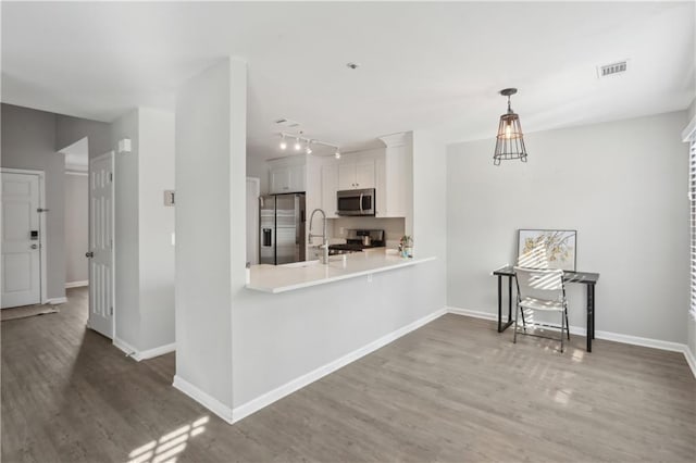 kitchen featuring appliances with stainless steel finishes, wood finished floors, a sink, white cabinets, and light countertops