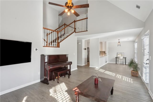 living area with high vaulted ceiling, wood finished floors, ceiling fan, baseboards, and stairway