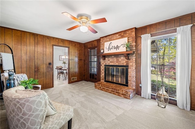 living room featuring wood walls, ceiling fan, a brick fireplace, and carpet floors