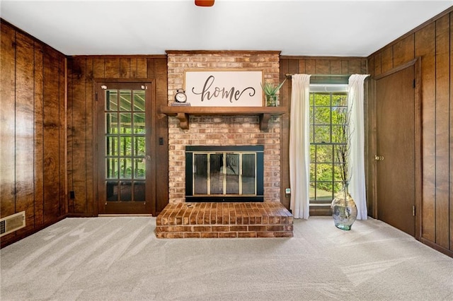 unfurnished living room with wooden walls, a fireplace, visible vents, and carpet floors