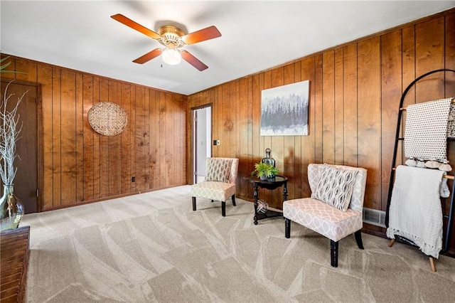 sitting room with wooden walls, a ceiling fan, and carpet floors
