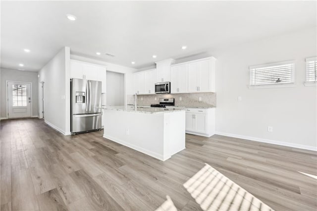 kitchen with appliances with stainless steel finishes, white cabinetry, light wood-style flooring, and backsplash