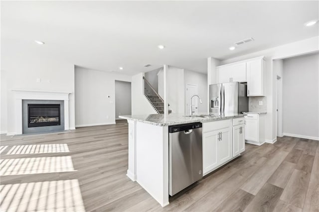 kitchen featuring a sink, light wood-type flooring, visible vents, light stone counters, and appliances with stainless steel finishes