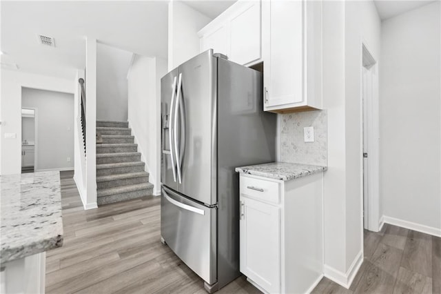 kitchen featuring stainless steel fridge, tasteful backsplash, light wood-style flooring, white cabinetry, and baseboards