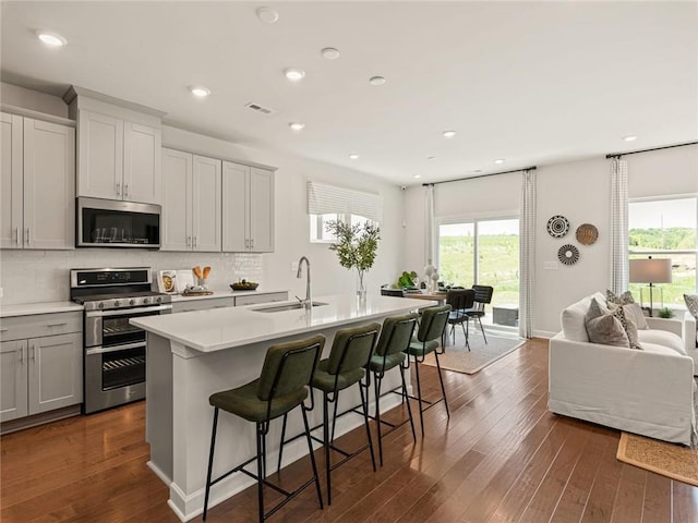 kitchen with a sink, appliances with stainless steel finishes, open floor plan, dark wood-style flooring, and backsplash