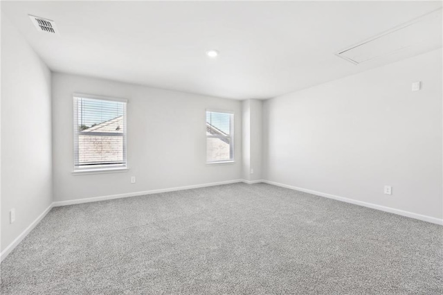 carpeted spare room with attic access, visible vents, baseboards, and plenty of natural light