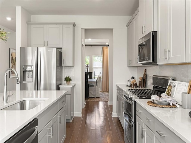 kitchen featuring a sink, stainless steel appliances, light countertops, dark wood-style flooring, and backsplash