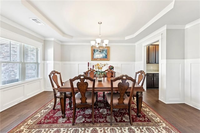 dining space featuring visible vents, dark wood-style flooring, a raised ceiling, a decorative wall, and a chandelier