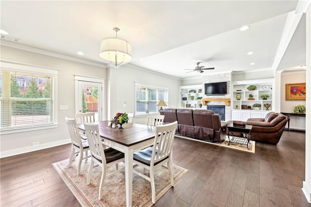 dining room with dark wood finished floors, crown molding, a ceiling fan, and a large fireplace