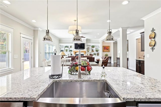 kitchen featuring open floor plan, light stone countertops, crown molding, and a sink