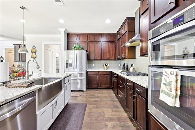 kitchen featuring a sink, backsplash, dark wood finished floors, appliances with stainless steel finishes, and wall chimney range hood