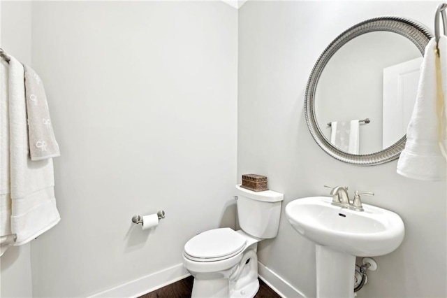 bathroom featuring toilet, wood finished floors, baseboards, and a sink