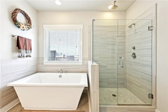 full bath featuring tile walls, wainscoting, a stall shower, and a freestanding bath