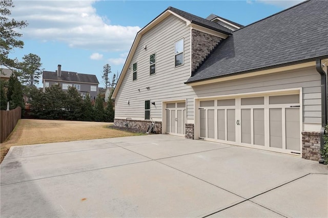 view of home's exterior featuring stone siding, a shingled roof, driveway, and fence