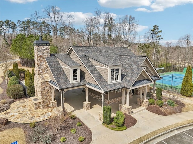 view of front of house with fence, stone siding, roof with shingles, and a chimney