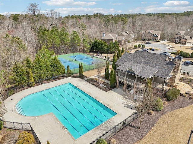 pool with a tennis court, a forest view, and fence