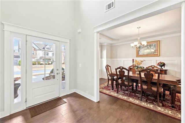 foyer with visible vents, dark wood-style flooring, ornamental molding, wainscoting, and a notable chandelier