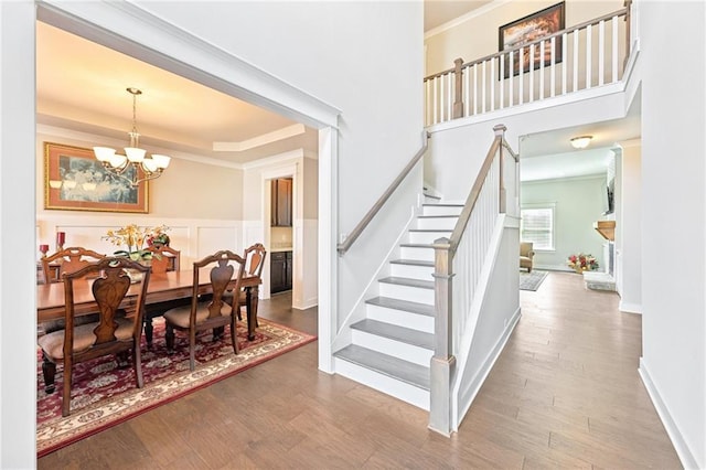 staircase with a raised ceiling, a notable chandelier, wood finished floors, and ornamental molding