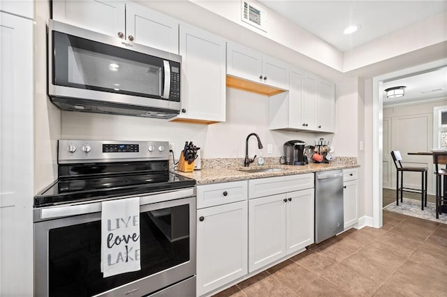 kitchen with stainless steel appliances, white cabinetry, sink, and light stone counters