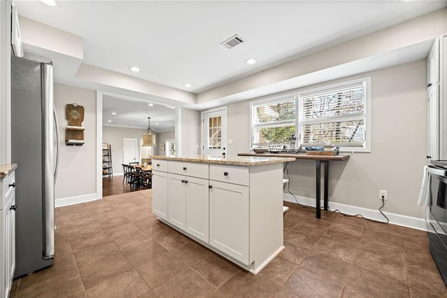 kitchen with white cabinets, a center island, stainless steel refrigerator, light stone countertops, and pendant lighting