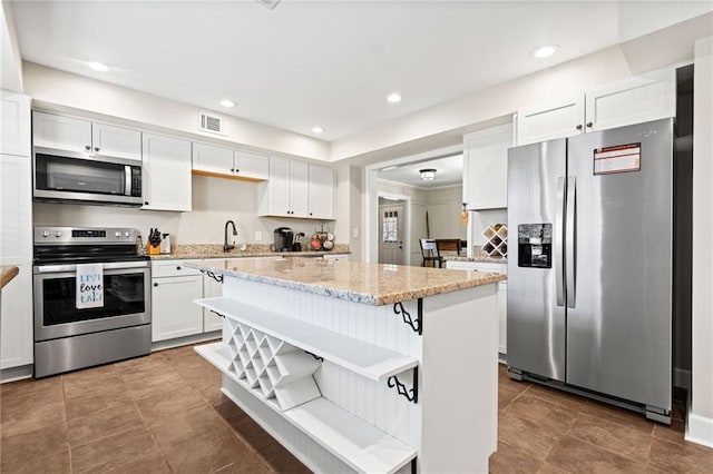 kitchen with appliances with stainless steel finishes, a center island, white cabinets, and light stone countertops