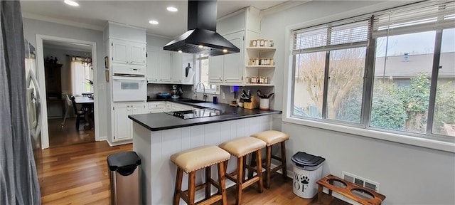 kitchen featuring oven, a peninsula, island exhaust hood, black electric cooktop, and a sink