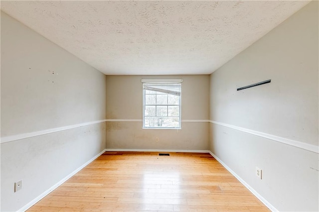 unfurnished room with a textured ceiling and light wood-type flooring