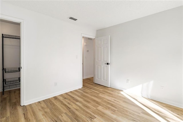 unfurnished bedroom featuring a walk in closet, light wood-type flooring, a closet, and a textured ceiling