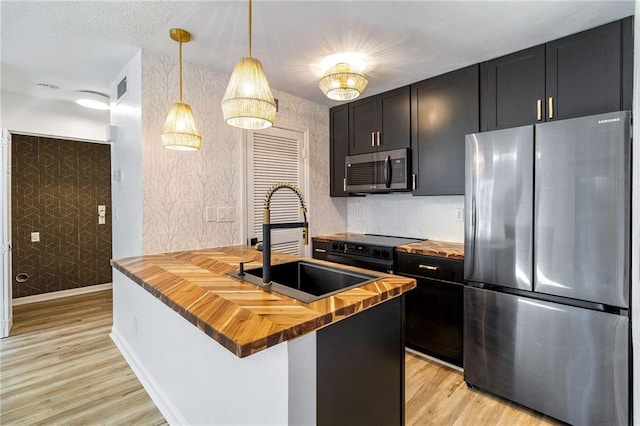 kitchen with a center island with sink, wooden counters, stainless steel appliances, pendant lighting, and sink