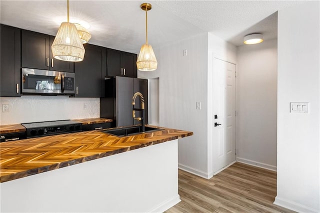 kitchen with decorative light fixtures, backsplash, appliances with stainless steel finishes, a textured ceiling, and wood counters