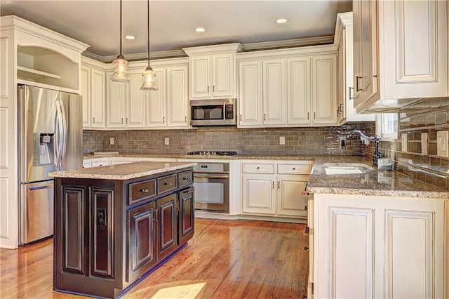 kitchen with light wood-style flooring, a kitchen island, appliances with stainless steel finishes, hanging light fixtures, and a sink