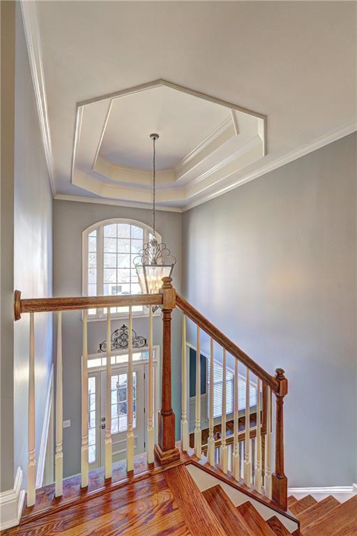 stairs featuring crown molding, a tray ceiling, wood finished floors, and a notable chandelier