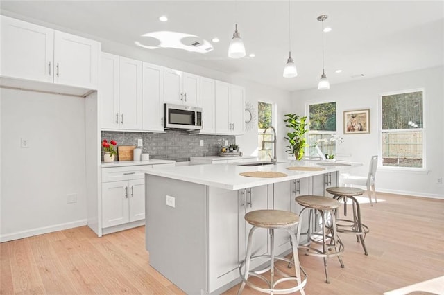 kitchen featuring sink, white cabinetry, hanging light fixtures, tasteful backsplash, and an island with sink